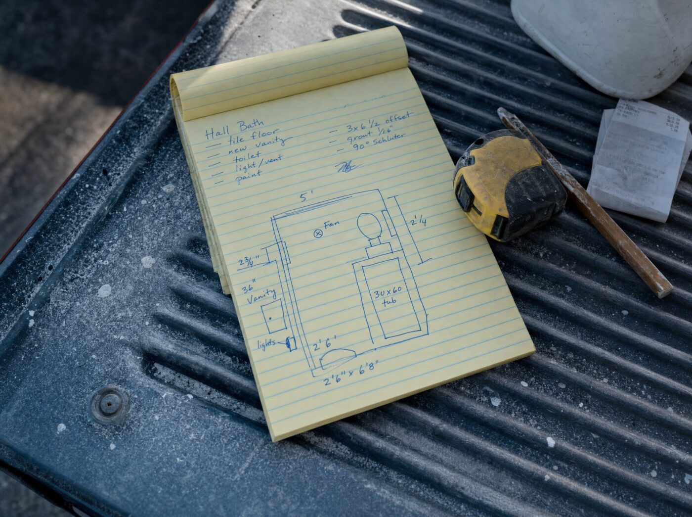 Handwritten bathroom remodel scope notes and a sketch on a legal pad, on the tailgate of a work truck